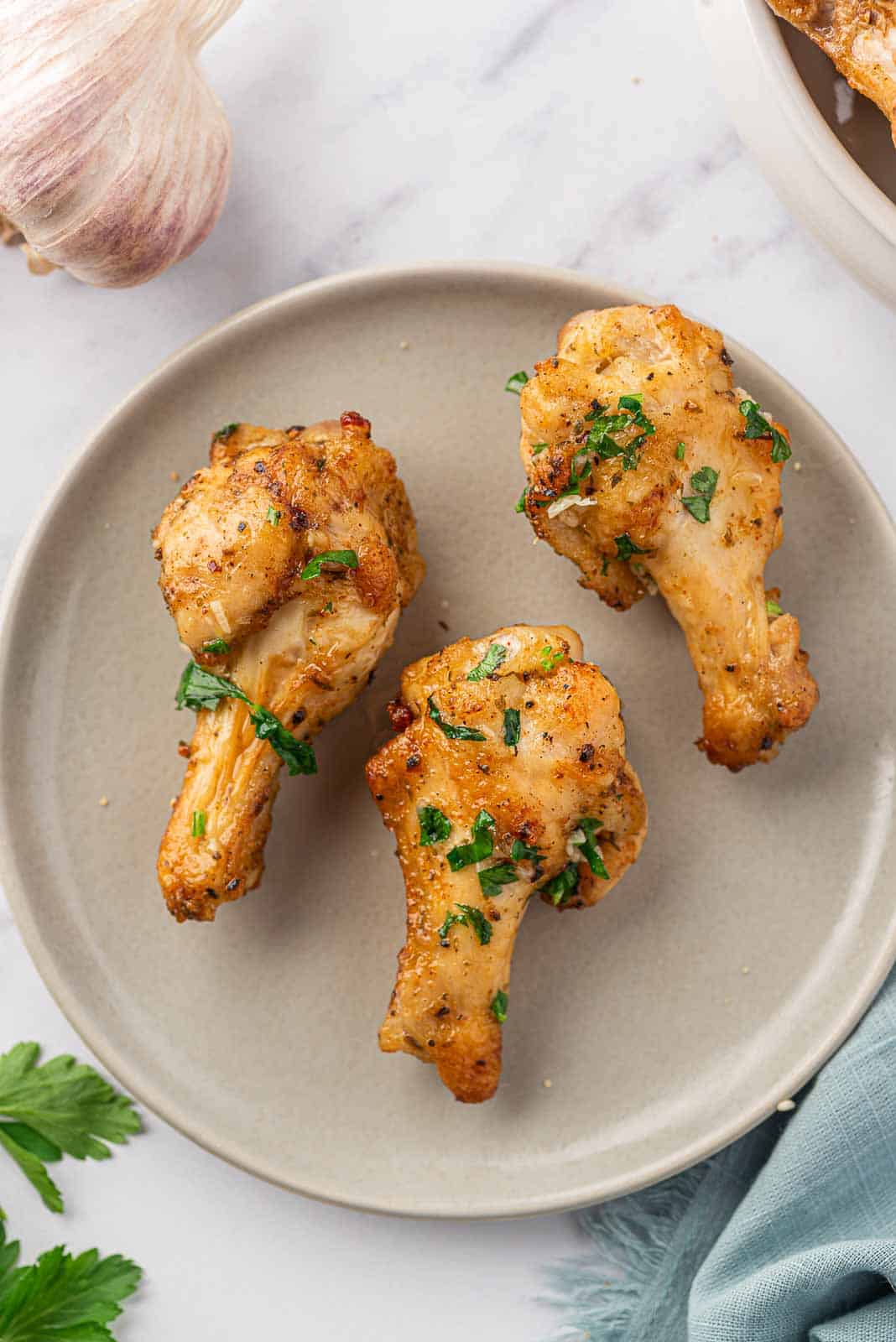 Three garlic chicken wings garnished with parsley rest on a plate.