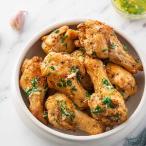 Air fryer garlic chicken wings in a serving bowl with garlic butter in the background.