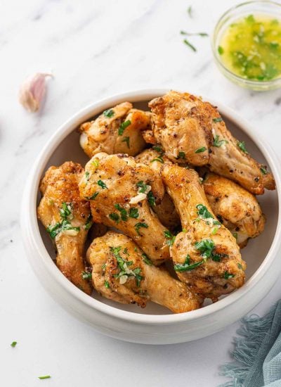 Air fryer garlic chicken wings in a serving bowl with garlic butter in the background.