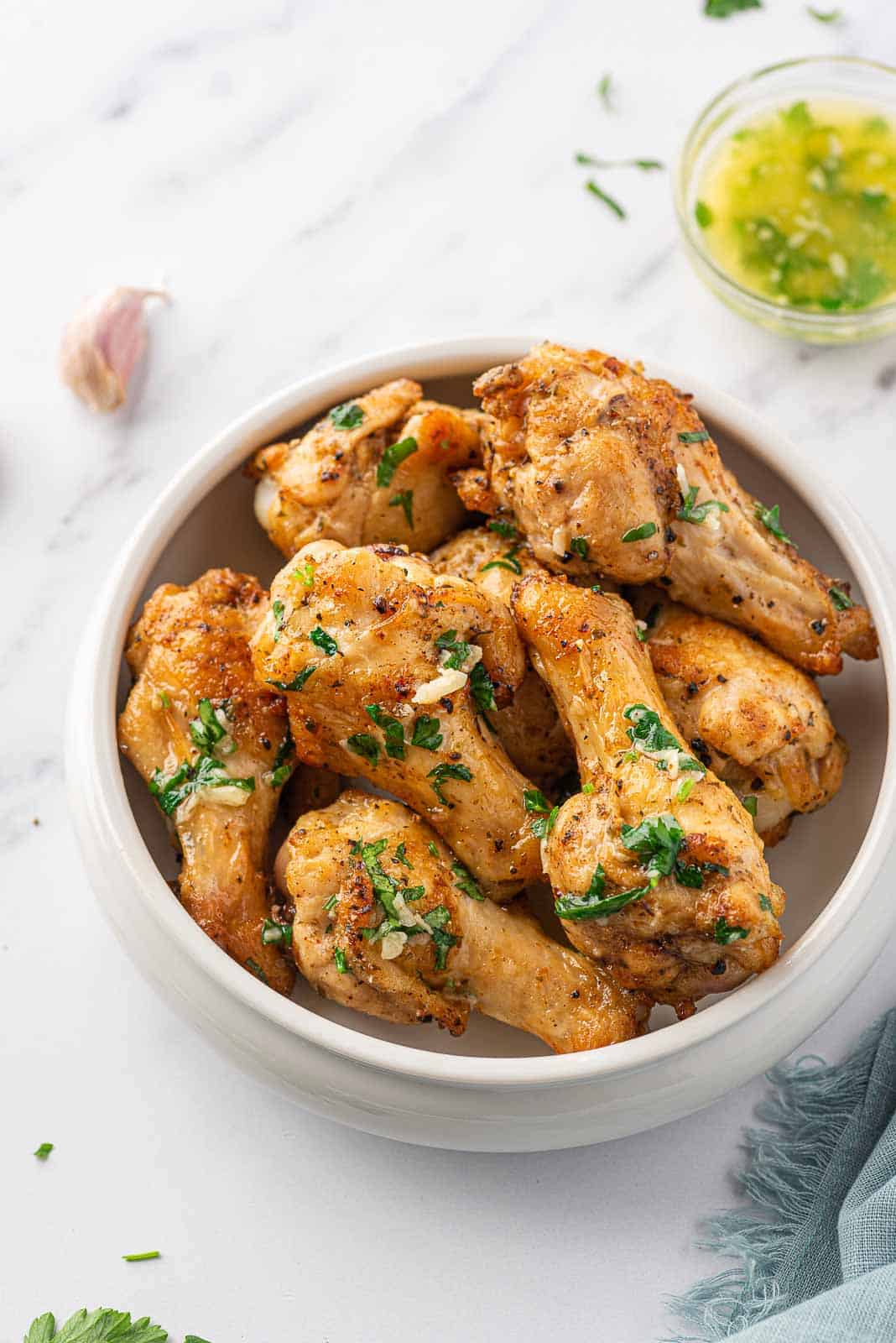 Air fryer garlic chicken wings in a serving bowl with garlic butter in the background.