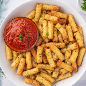 A plate of air fried pasta with a small bowl of marinara sauce.