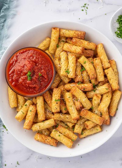 A plate of air fried pasta with a small bowl of marinara sauce.