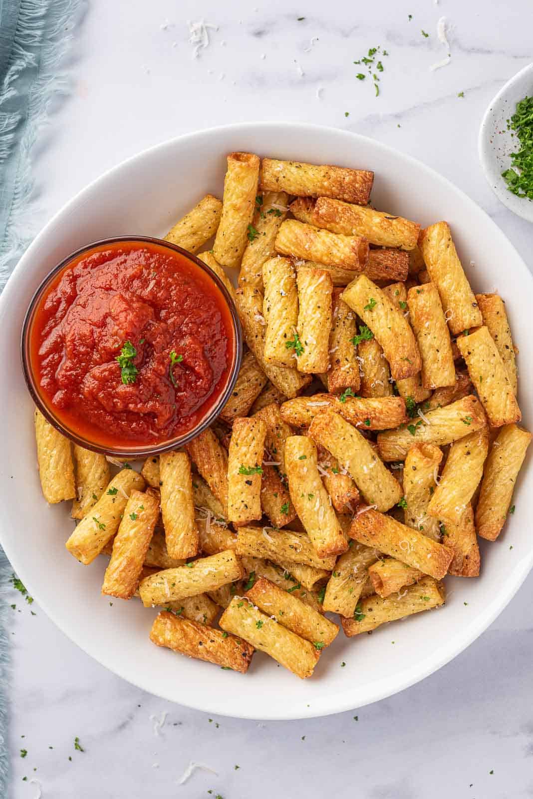 A plate of air fried pasta with a small bowl of marinara sauce.