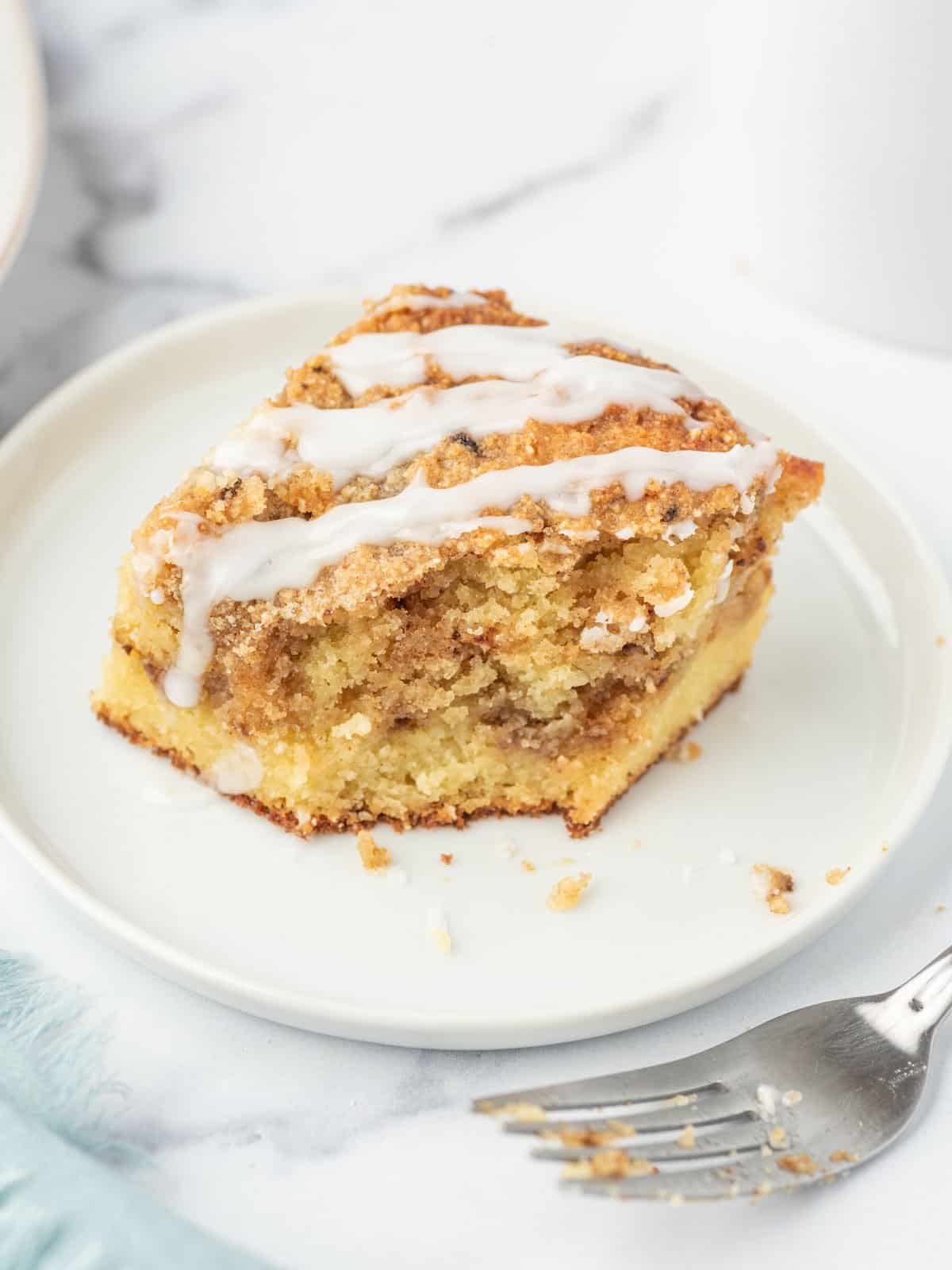 A piece of low carb coffee cake with a bite missing sits on a white plate with a few crumbs. A fork with crumbs sits to the side.