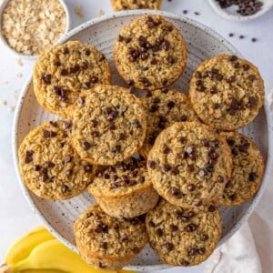 Overhead view of a plate of baked banana oatmeal cups with ingredients scattered around.