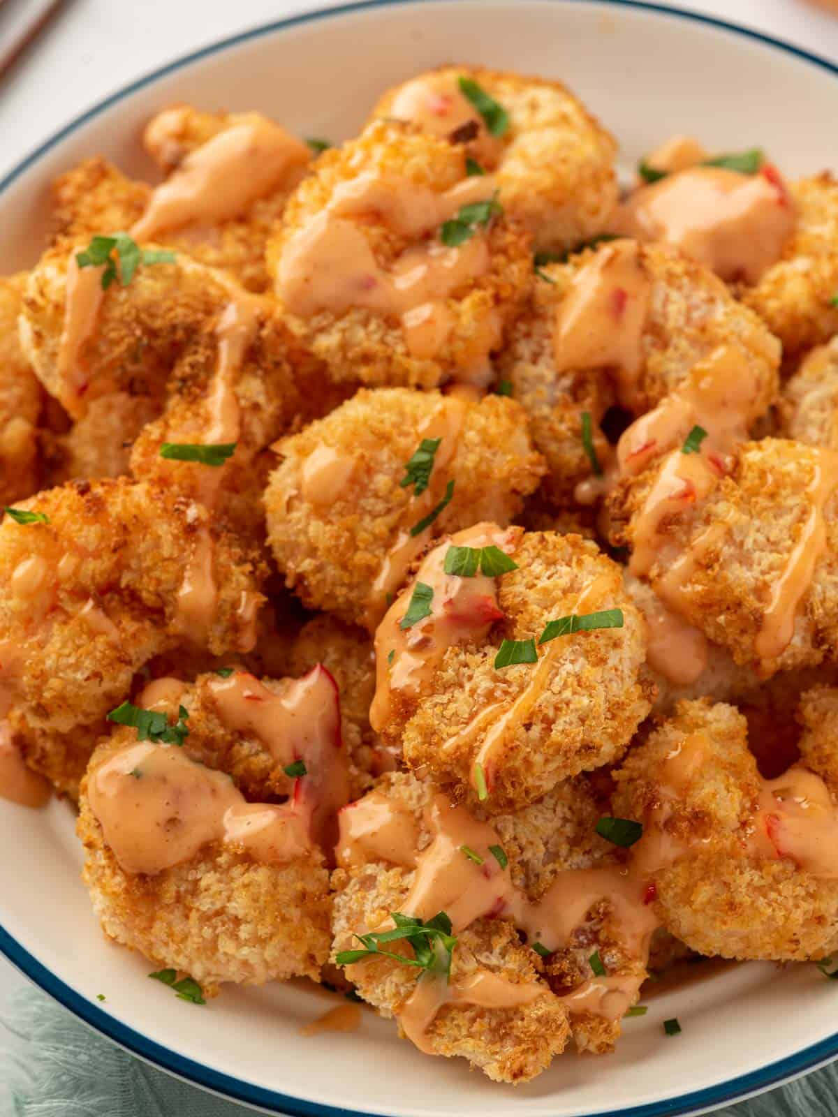 A plate of crispy air fryer panko shrimp drizzled with bang bang sauce.