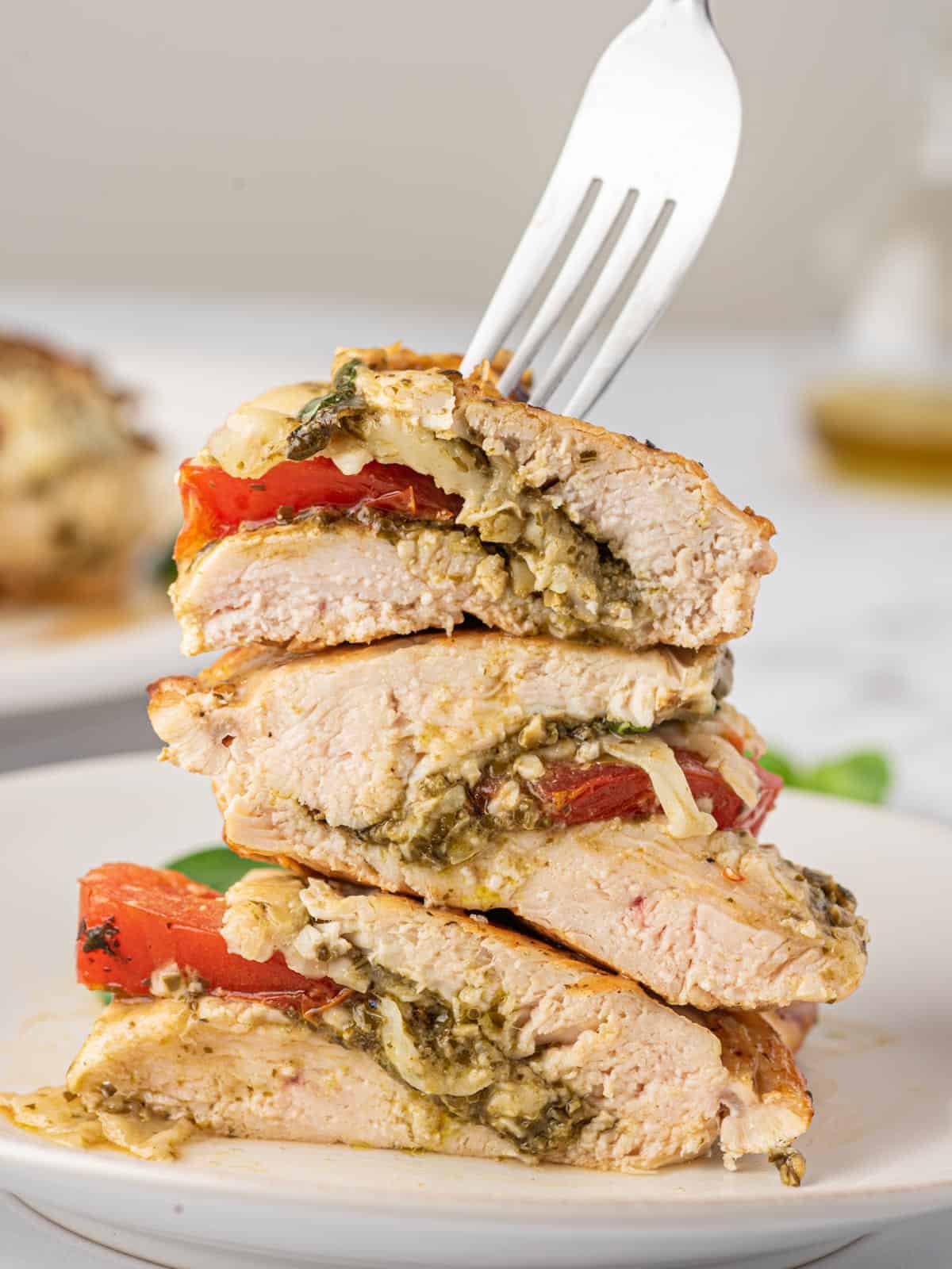 A fork holds stuffed Pesto mozzarella chicken breasts sliced in half and piled on a plate.