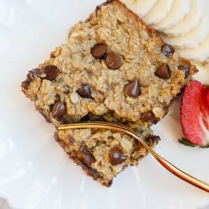 A plate with chocolate chip baked oats, fruit and a fork.