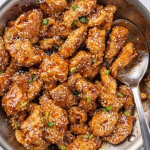 A pan of crispy honey sesame chicken with a spoon.