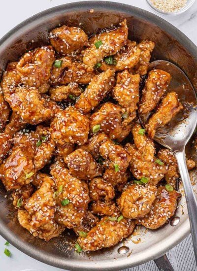 A pan of crispy honey sesame chicken with a spoon.