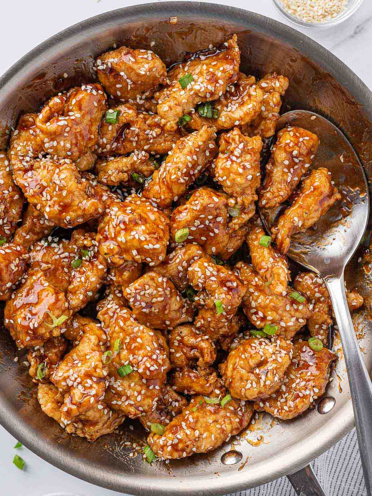 A pan of crispy honey sesame chicken with a spoon.