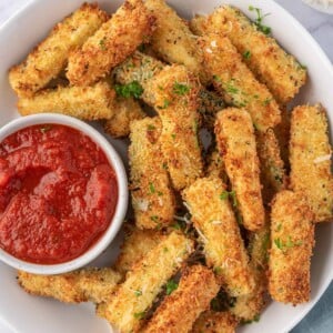 Air fryer zucchini sticks on a plate with a bowl of marinara.