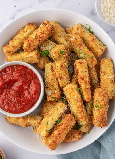 Air fryer zucchini sticks on a plate with a bowl of marinara.