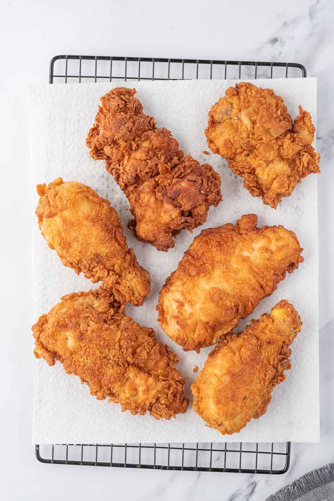 Extra crispy fried chicken draining on paper towels on a wire rack.