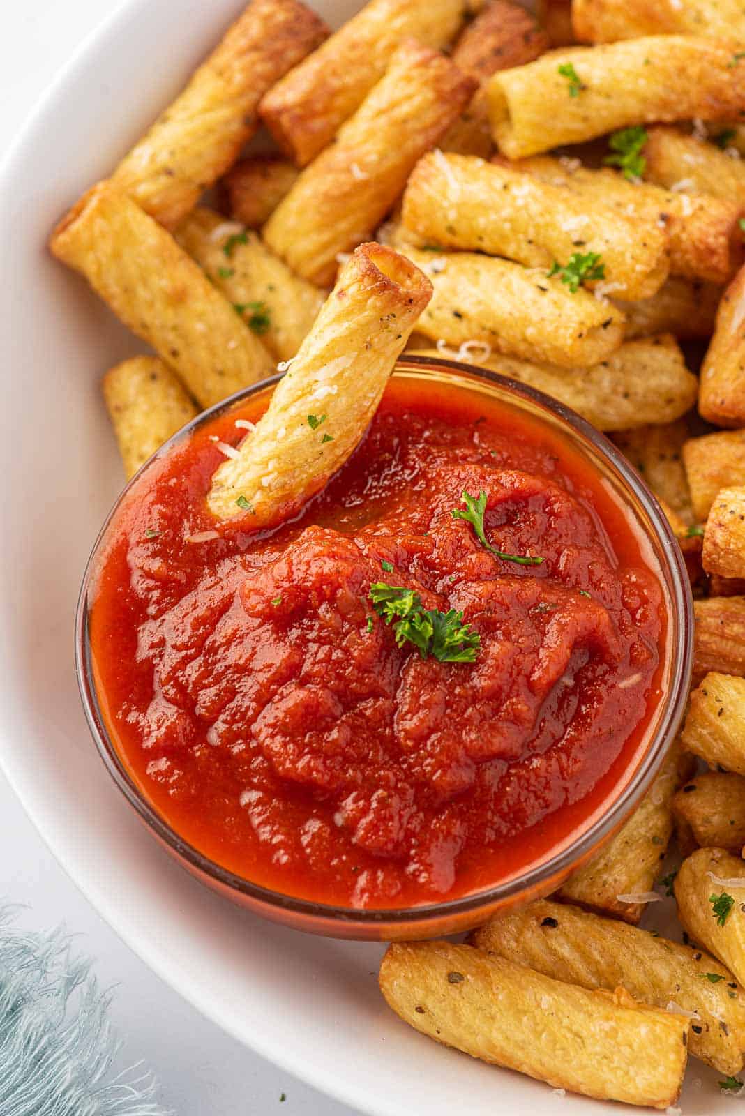 A plate of fried pasta chips and one fried noodle dipping into marinara sauce.