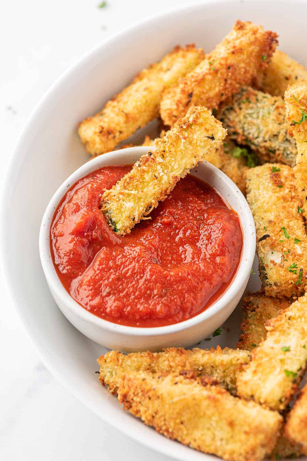 A plate of crispy zucchini fries with one zucchini dunked in marinara.