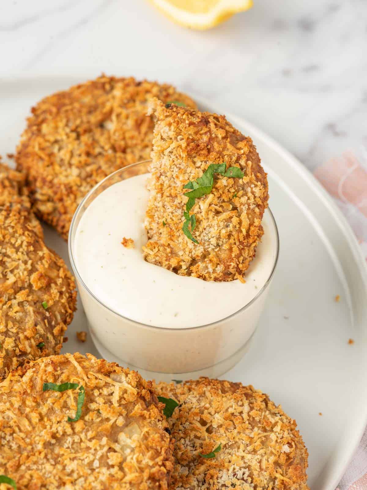 A piece of air fryer tuna patties is dunked into dip.