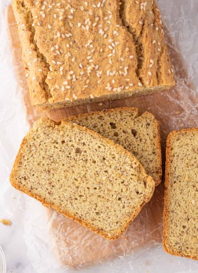 A loaf of keto sandwich bread with several slices of bread rest on a bread board.