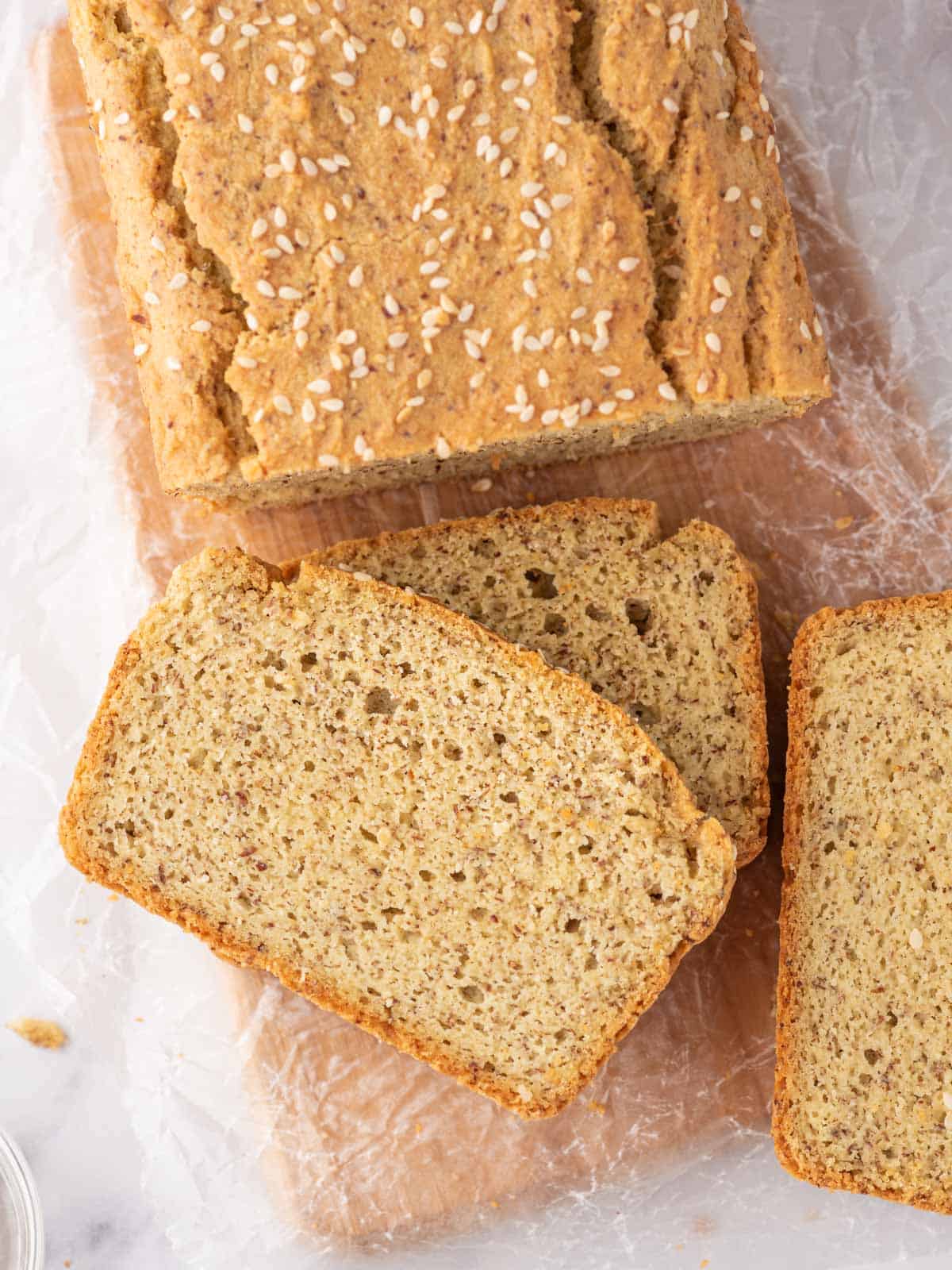 A loaf of keto sandwich bread with several slices of bread rest on a bread board.