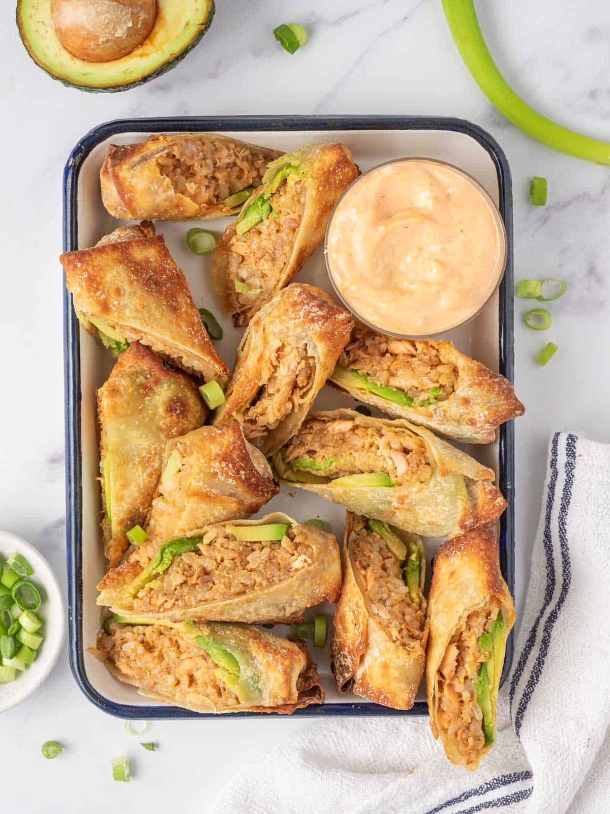 Spicy Salmon and Rice Egg Rolls cut in half and served on a tray with dipping sauce.