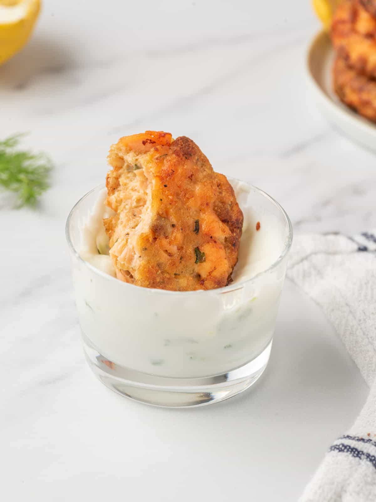 A bite of Salmon patties with bread crumbs being dunked in tzatziki sauce.