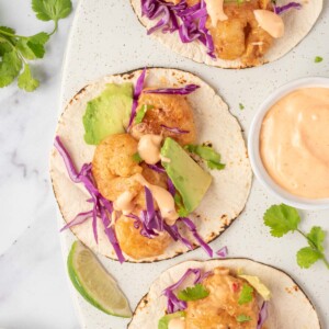 Three bang bang shrimp tacos with dynamite sauce sit on a serving platter.