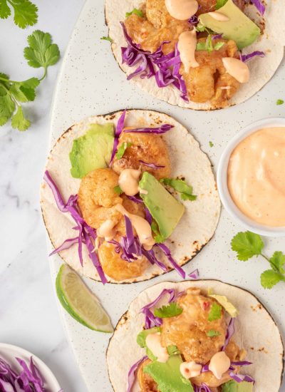 Three bang bang shrimp tacos with dynamite sauce sit on a serving platter.