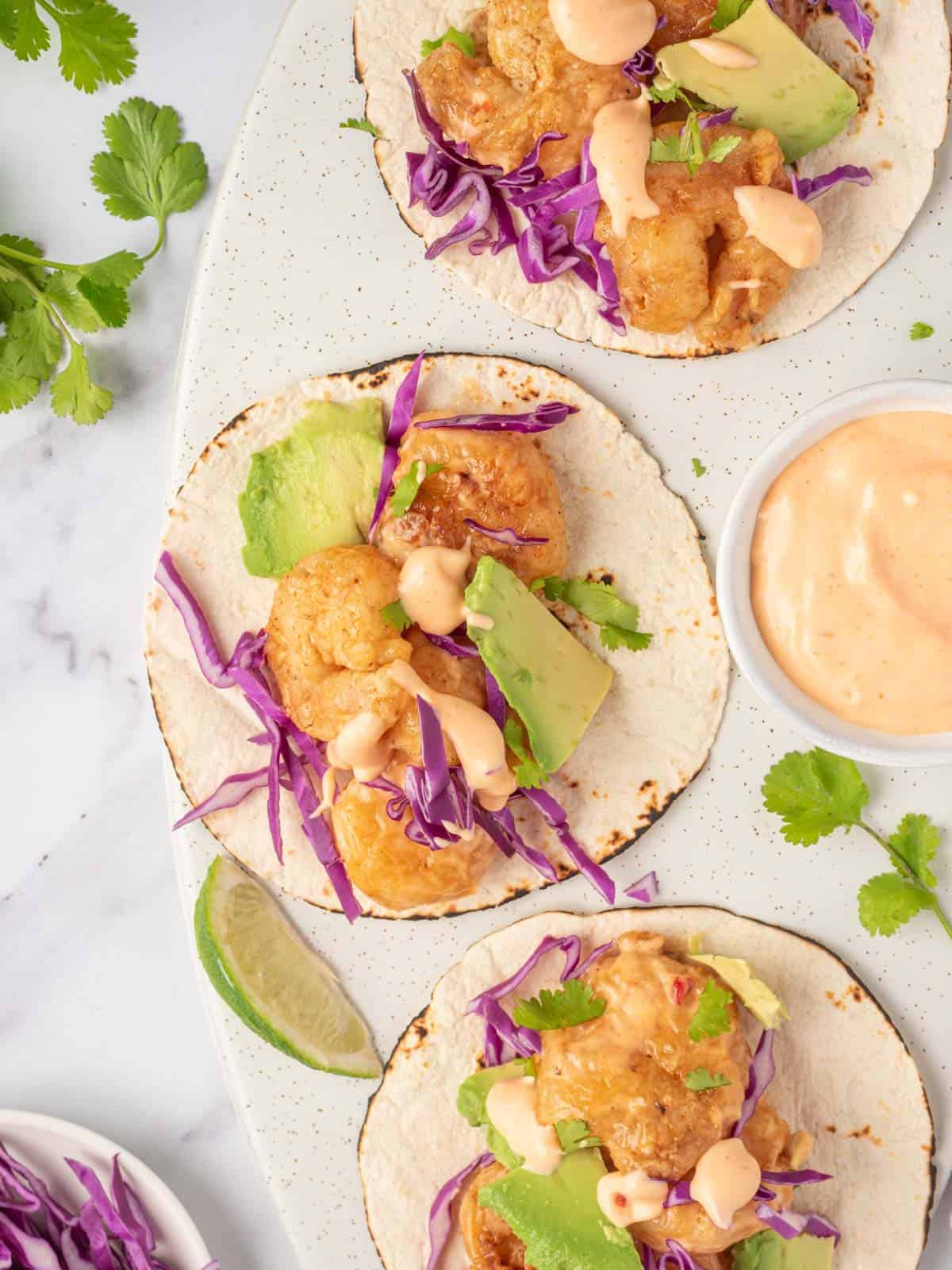 Three bang bang shrimp tacos with dynamite sauce sit on a serving platter.