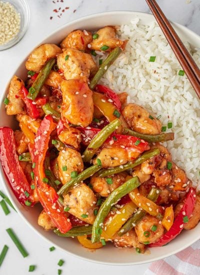 Sweet Thai chili chicken stir fry on a plate with rice and chopsticks.