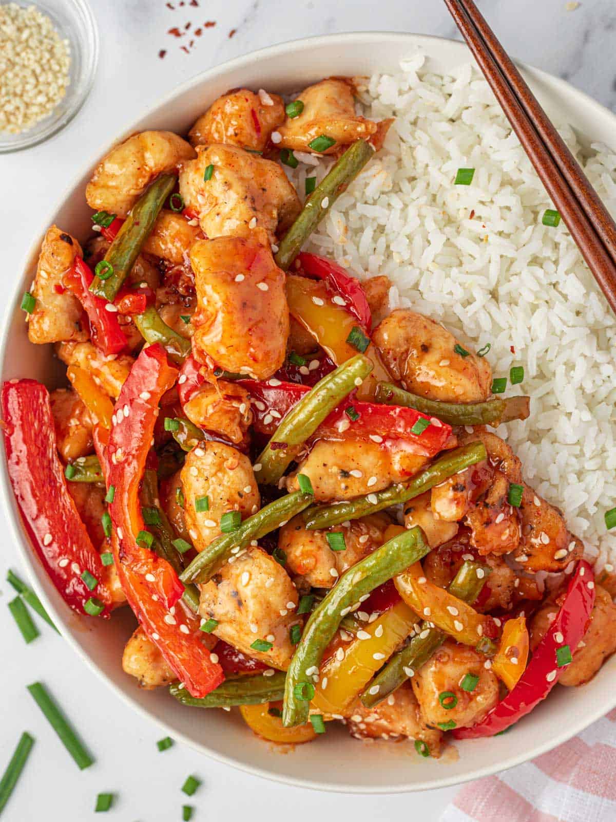 Sweet Thai chili chicken stir fry on a plate with rice and chopsticks.