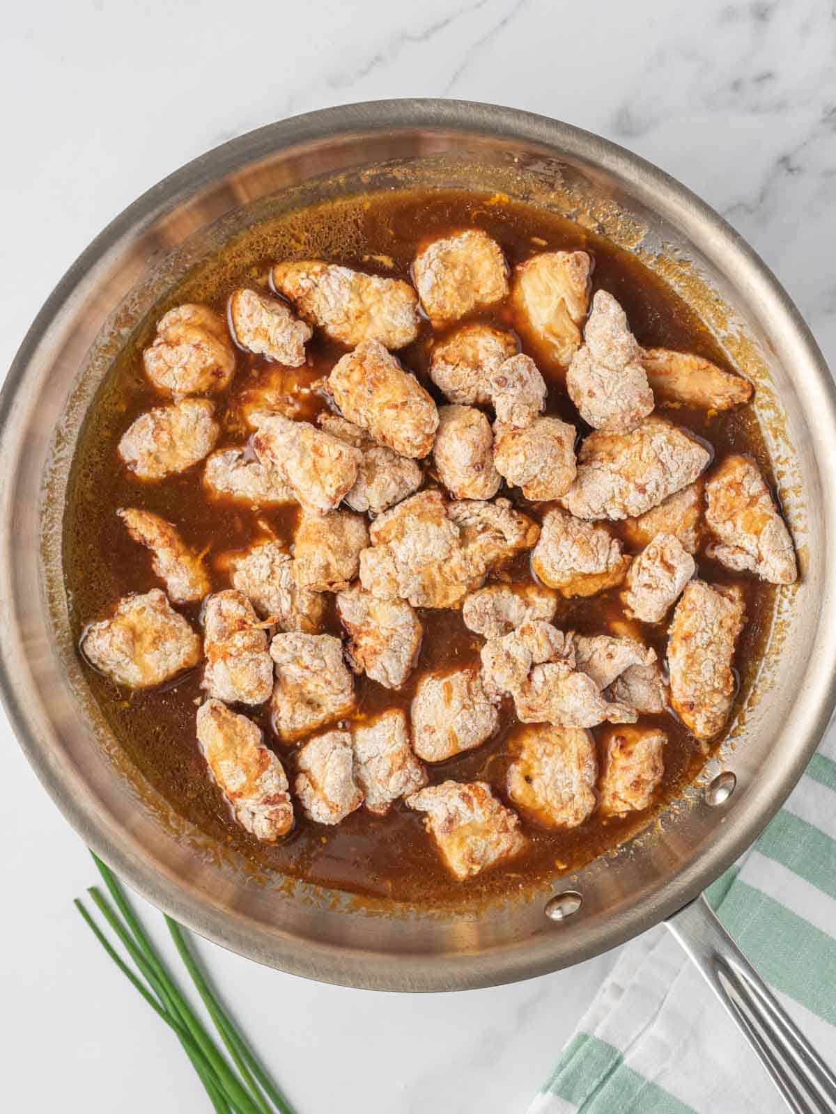 Tossing crispy chicken with the easy orange chicken sauce in a skillet.