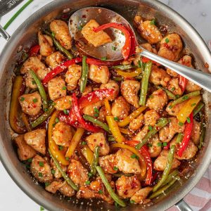 Crispy chicken stir fry in a skillet with a spoon for serving.