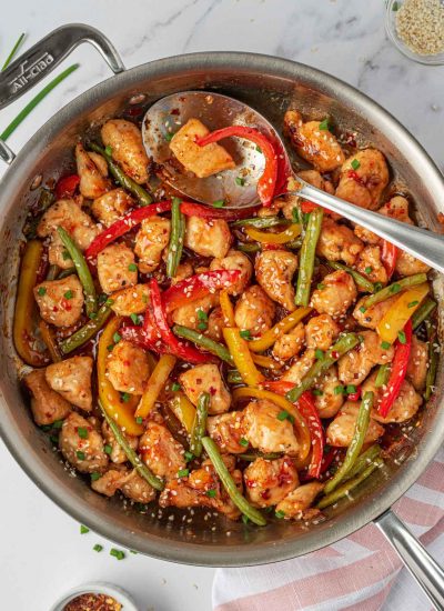 Crispy chicken stir fry in a skillet with a spoon for serving.