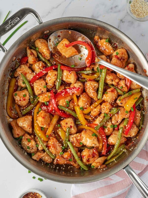 Crispy chicken stir fry in a skillet with a spoon for serving.