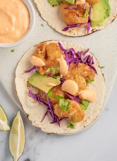 An assembled spicy shrimp taco with bang bang sauce sits on a serving platter.