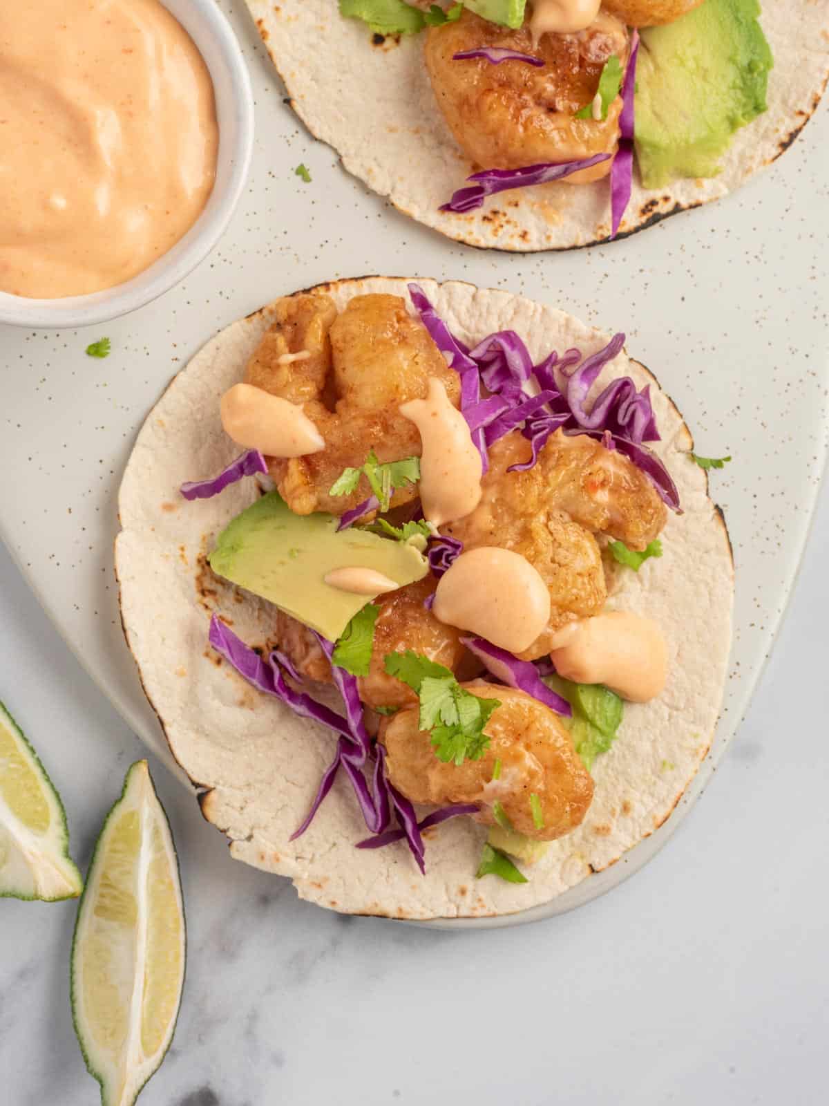 An assembled spicy shrimp taco with bang bang sauce sits on a serving platter.