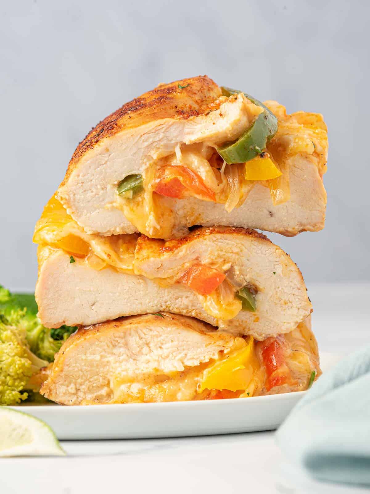 A stack of fajita stuffed chicken sliced in half on a plate with cheese oozing out.