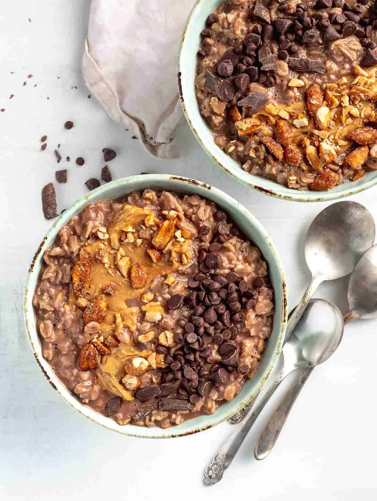two chocolate bowls of oats topping with nuts and chocolate chips