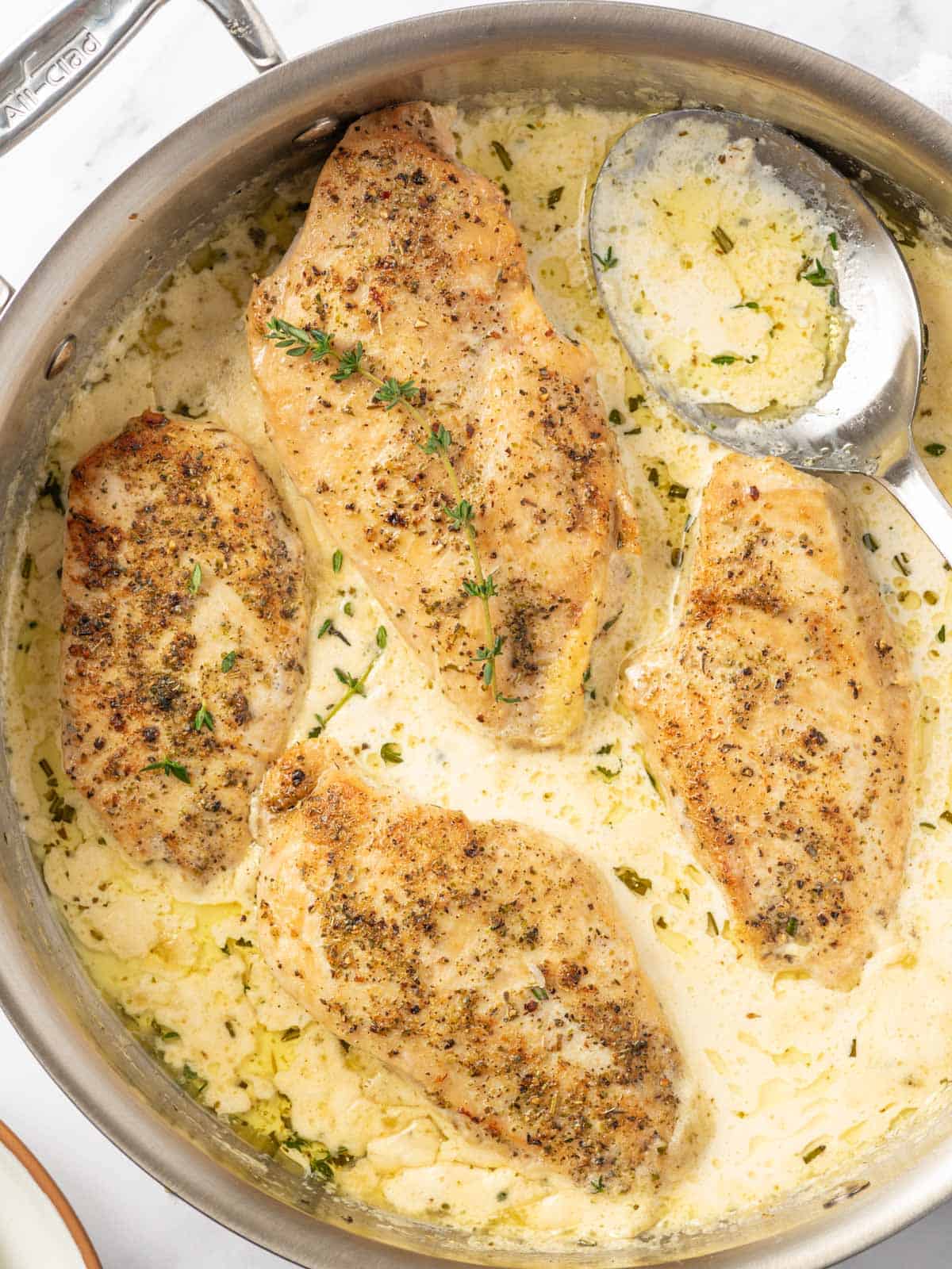 A spoon scoops creamy herb sauce for chicken in a skillet.