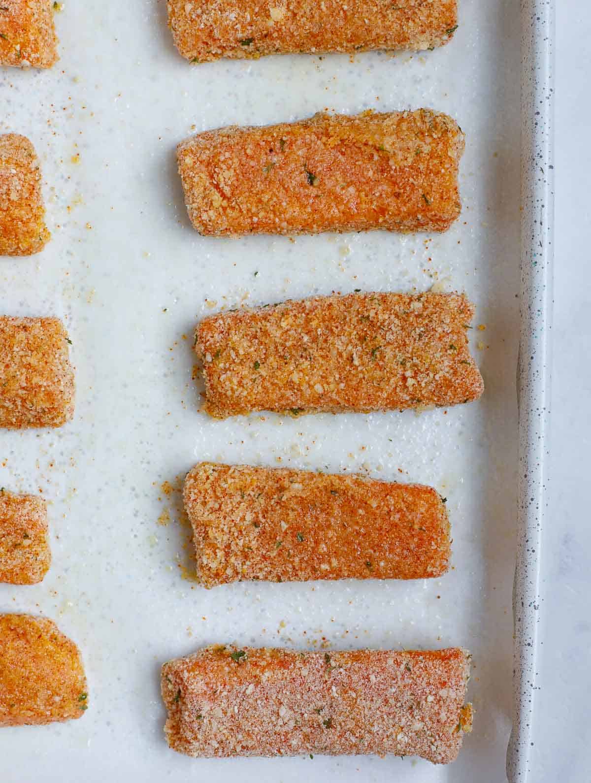 Salmon fish sticks ready to be baked on a tray.