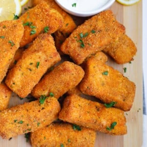 Crispy salmon fish fingers on a board with dipping sauce.