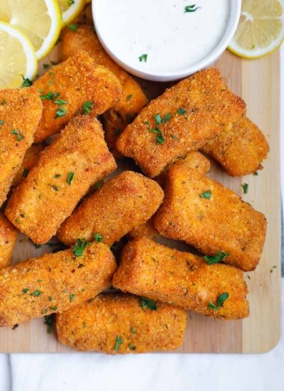 Crispy salmon fish fingers on a board with dipping sauce.