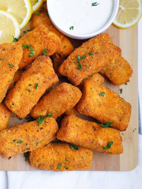 Crispy salmon fish fingers on a board with dipping sauce.