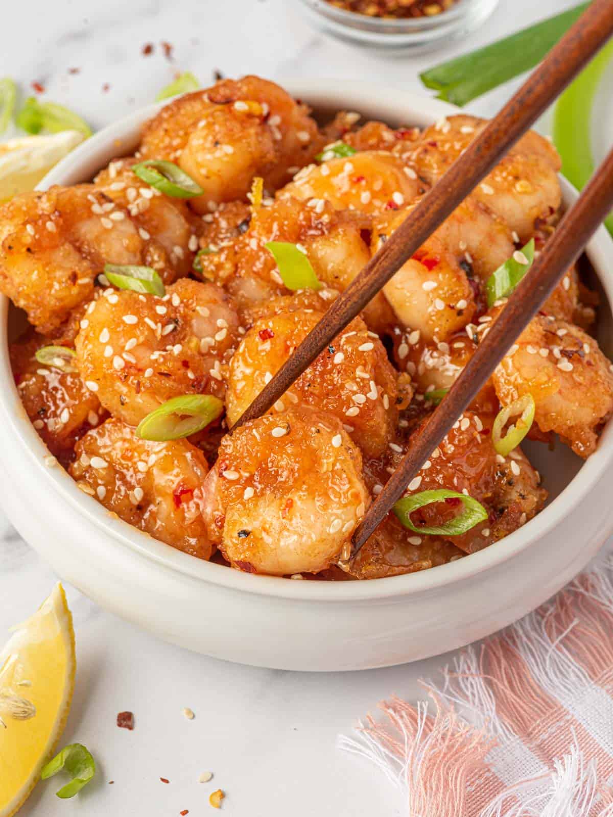 Spicy fried shrimp with firecracker shrimp sauce in a bowl with a piece being picked up by chopsticks.