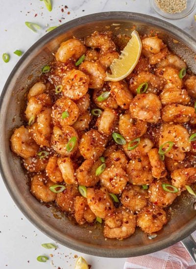 Garnished firecracker shrimp in a skillet with a lemon wedge.