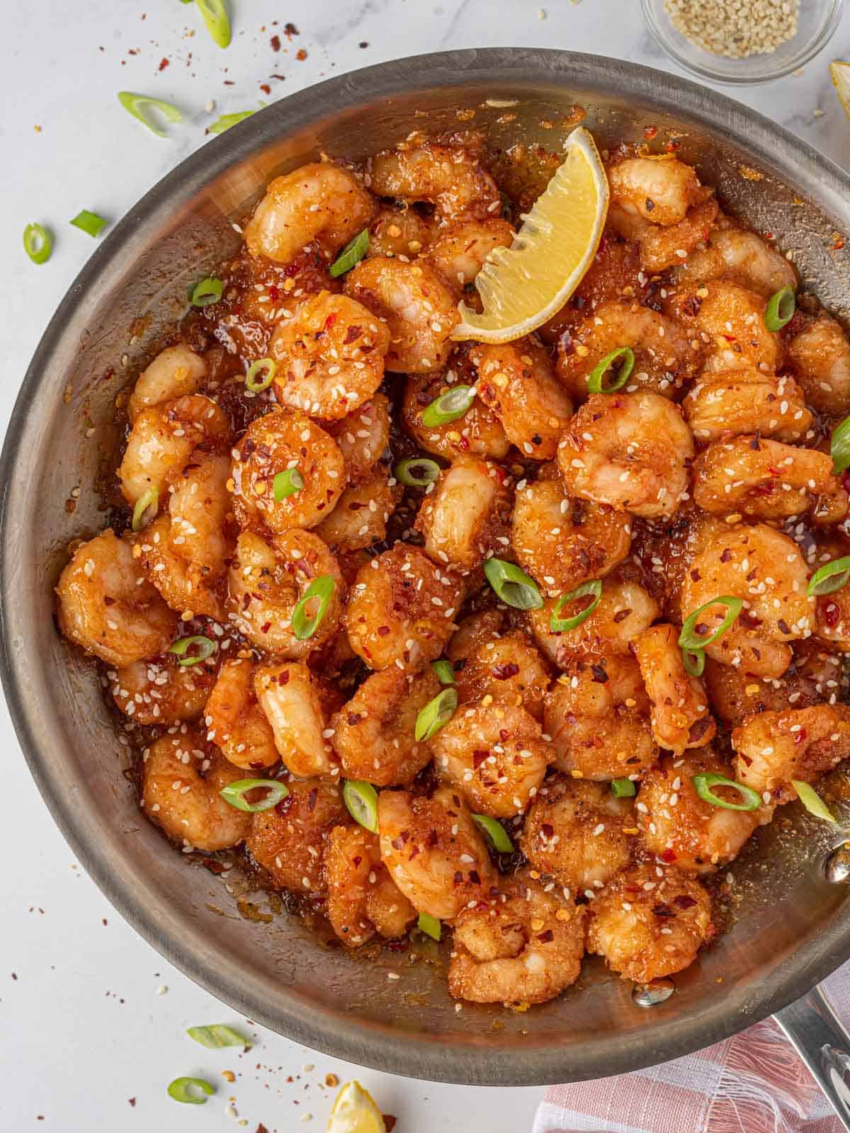 Garnished firecracker shrimp in a skillet with a lemon wedge.