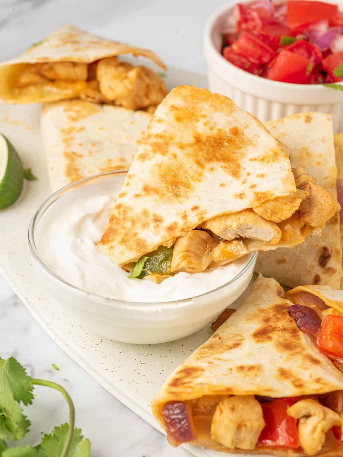 A triangle of chicken and cheese quesadilla being dipped into sour cream.