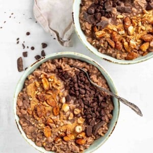 two chocolate bowls of oats topping with nuts and chocolate chips