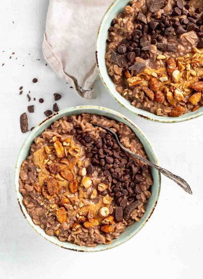 two chocolate bowls of oats topping with nuts and chocolate chips