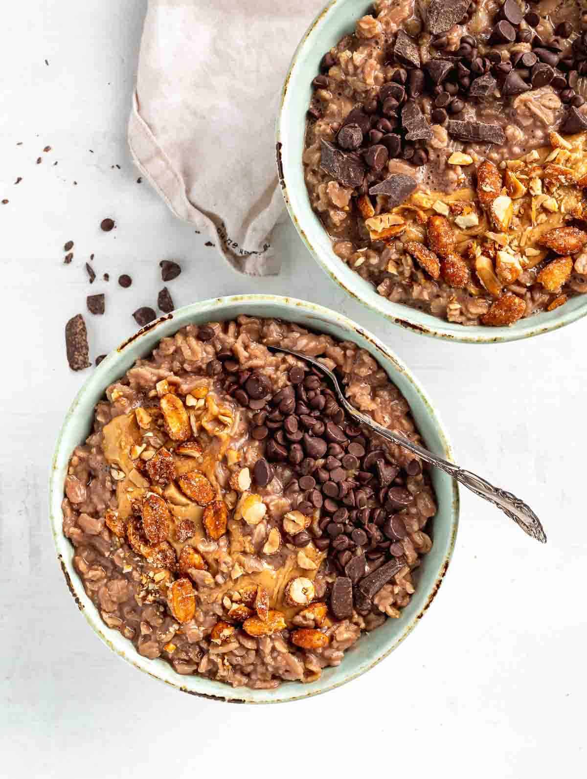 two chocolate bowls of oats topping with nuts and chocolate chips